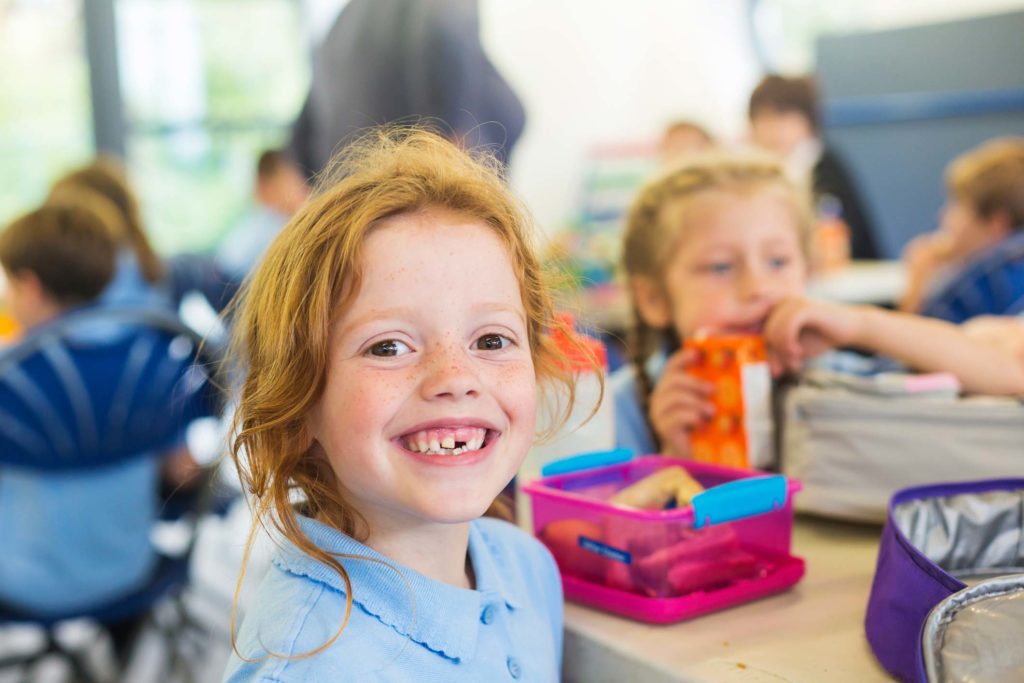 Little girl smiling with other students in background at canteen